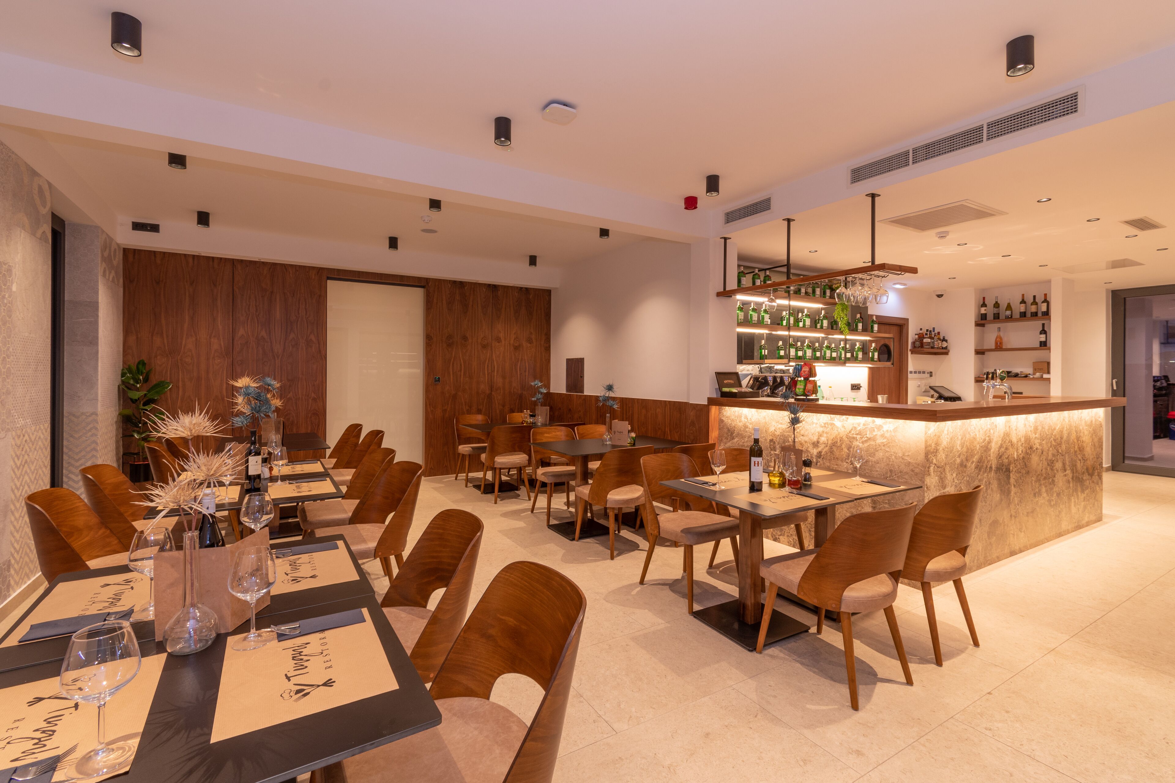 A modern restaurant with wooden furniture, a bar area, and a wine display.
