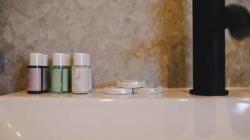 A bathroom with a marble wall, a black faucet, and three bottles of liquid soap on a white sink.