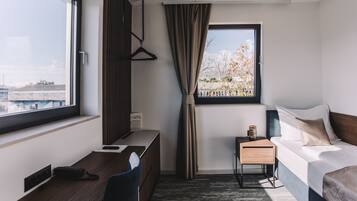 Una habitación de hotel con una cama, un escritorio, una silla, una mesita y una ventana que ofrece vistas a edificios, además de una cortina.
