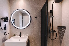 A bathroom with a round mirror, a sink, a handheld showerhead, and a towel rack.