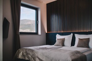 A hotel room with a large bed, a window with curtains, and a view of the mountains.