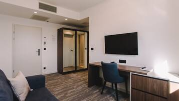 Een moderne kamer met een donkerblauwe bank, een houten bureau, een stoel en een flatscreen televisie aan de muur.
