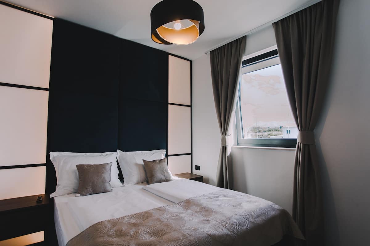 A neatly made bed with a patterned bedspread, a dark headboard, and a bedside table with a lamp.