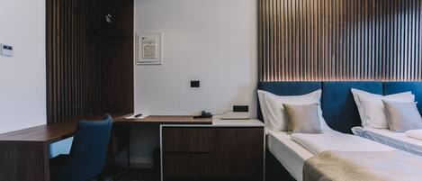 A hotel room with a desk, a bed with blue headboard, and a wooden slat wall design.