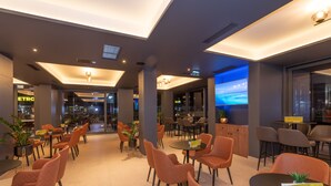 Un espace intérieur moderne doté de coins salon, d’un bar et d’un grand écran diffusant un paysage pittoresque.