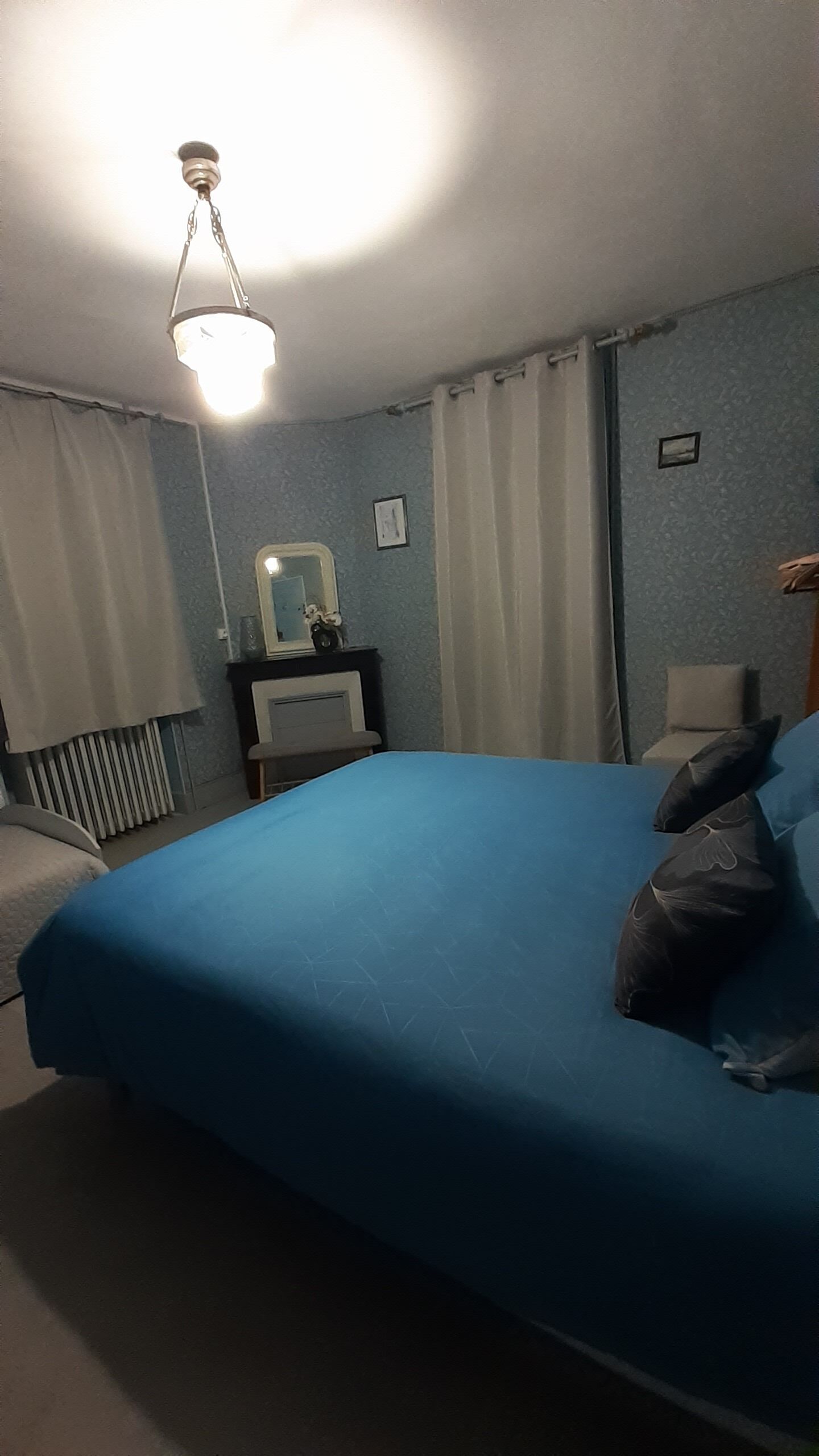 Et soveværelse med seng, natbord, spejl og radiator.