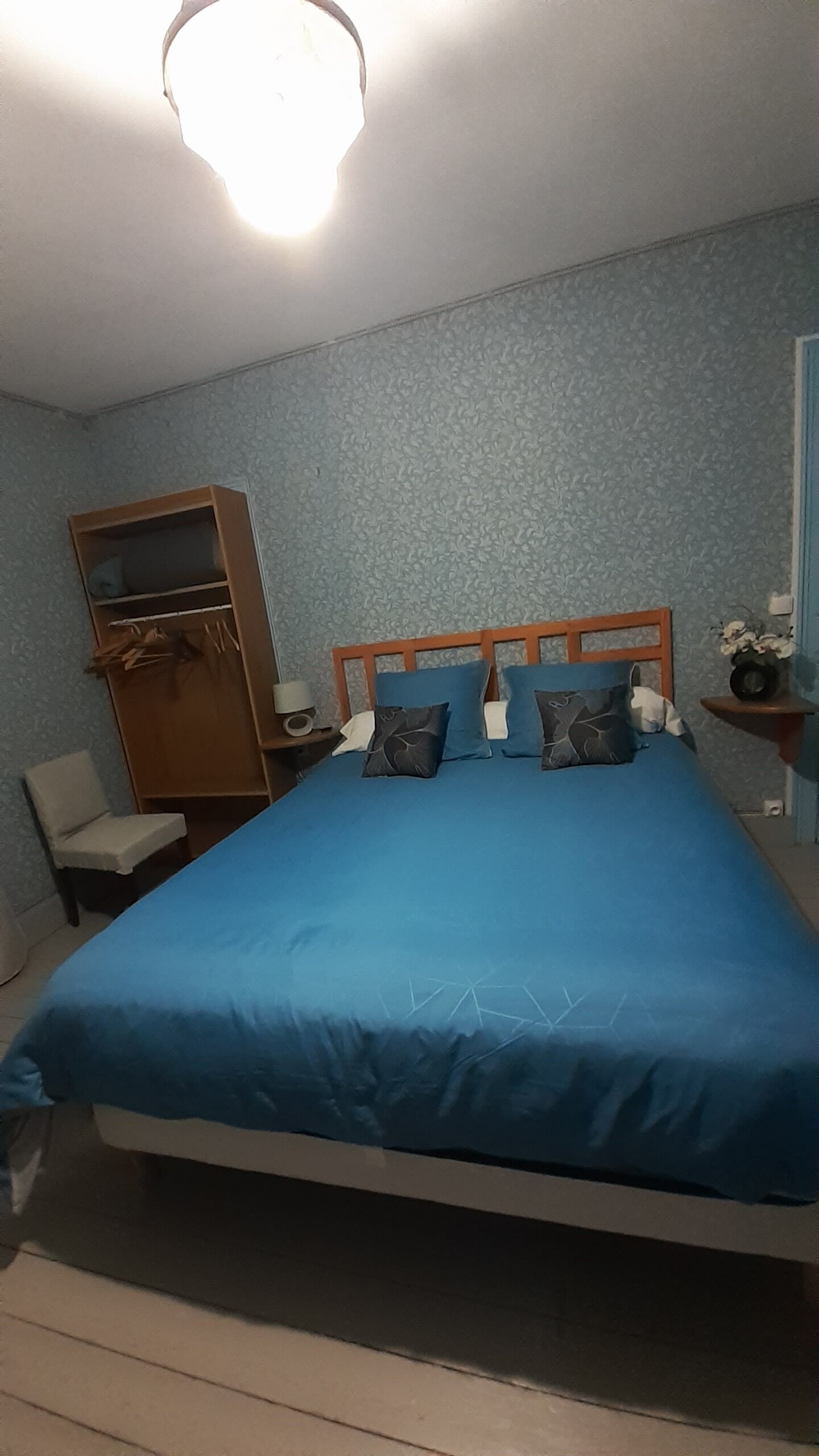 Un dormitorio con una cama, un armario de madera, una silla y una mesita de noche con lámpara.