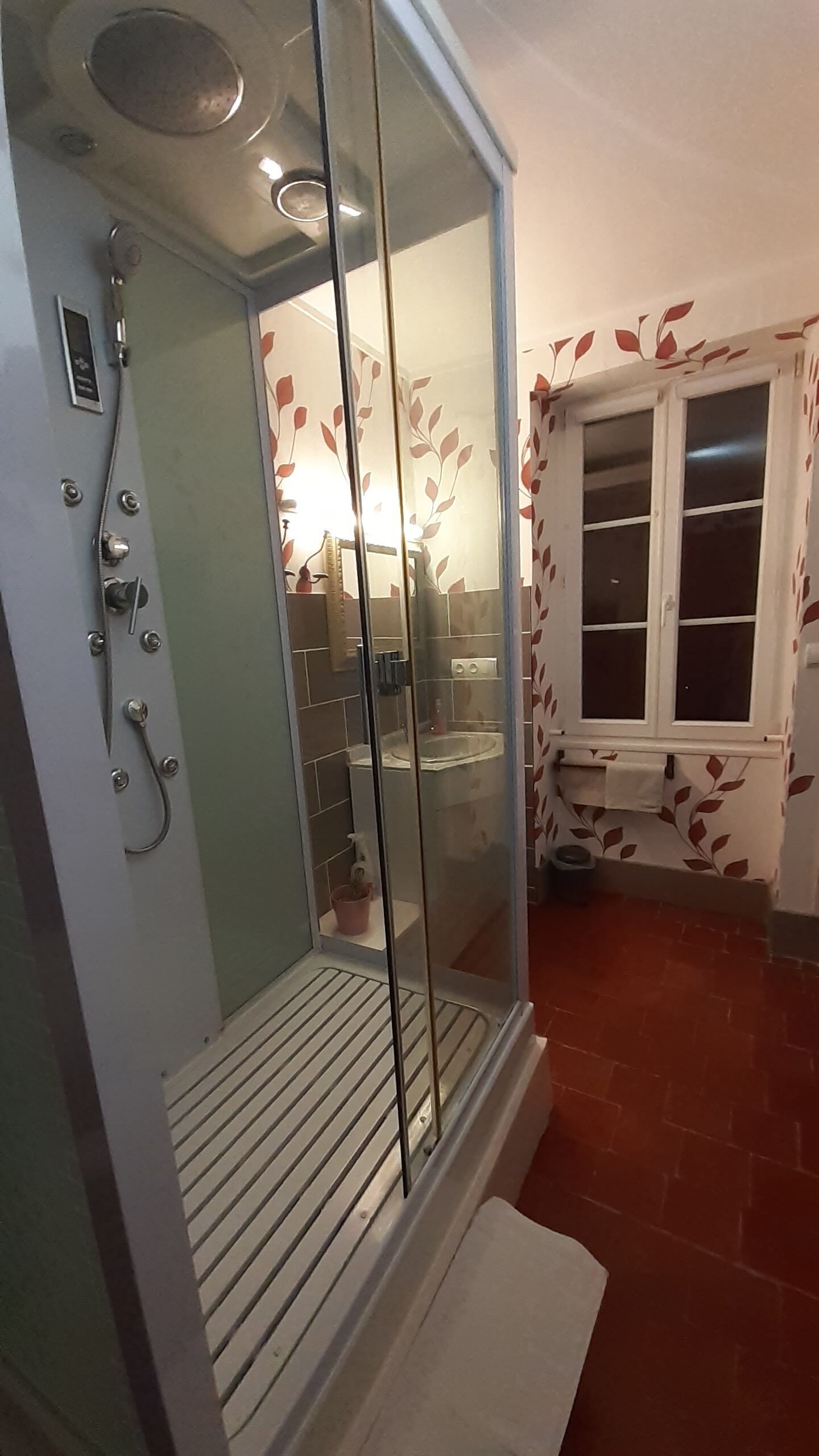 A bathroom with a glass shower enclosure, a toilet, and a window with a leaf pattern.