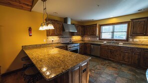 Une cuisine dotée de plans de travail en granit, de meubles en bois, d’une cuisinière en acier inoxydable et d’une fenêtre avec des stores.