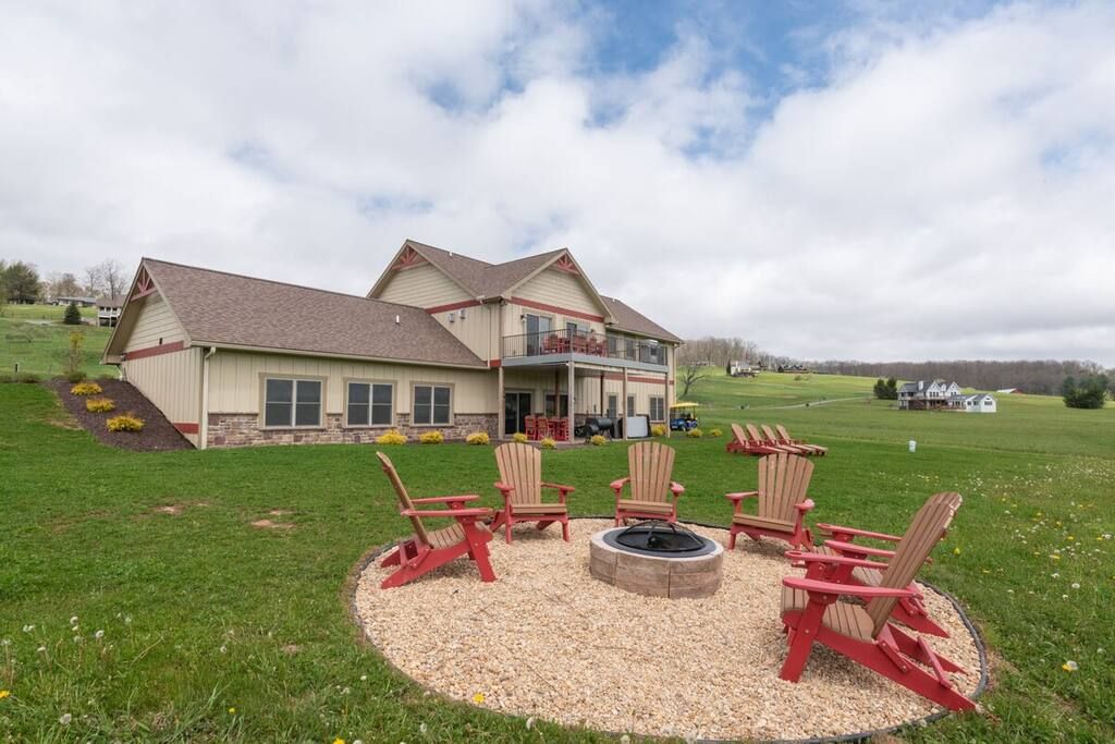 A two-story house with a covered porch and a fire pit area with Adirondack chairs.