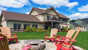 A two-story house with a front porch, a fire pit, and red Adirondack chairs. - 6BR Luxury Escape w/ Indoor Pool Boat Dock Avail (Swanton)