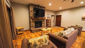 A living room with a stone fireplace, wooden furniture, and a flat-screen TV. - 6BR Luxury Escape w/ Indoor Pool Boat Dock Avail (Swanton)