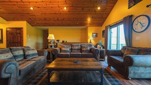 A cozy living room with a wooden ceiling, a large window with curtains, and a map on the wall. - 6BR Luxury Escape w/ Indoor Pool Boat Dock Avail (Swanton)