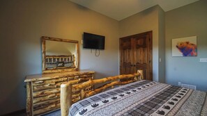 A bedroom with a wooden bed, a dresser, a television on the wall, and a door.