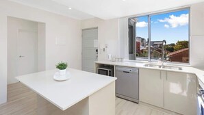 Cozinha moderna com bancada branca, máquina de lavar louça e janela com vista para edifícios.