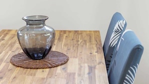 Uma mesa de jantar de madeira com um vaso de vidro e um jogo americano trançado.