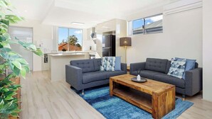 Uma sala de estar moderna com dois sofás cinzas, uma mesa de centro de madeira e um tapete azul.