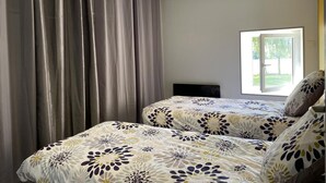 A bedroom with two beds, grey curtains, and a window with a view of greenery.