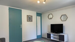 A modern living room with teal and white walls, a flat-screen TV on a white cabinet, and a small table with three stools.