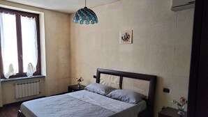 Un dormitorio con cama, mesita de noche, ventana con cortinas, aire acondicionado instalado en la pared y una obra de arte en la pared.