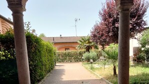 Un sendero pavimentado que conduce a un edificio con tejado de baldosas, rodeado de vegetación y un arco de ladrillo.