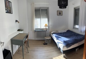 Una camera da letto con un letto, una scrivania, una sedia, un termosifone e una finestra con persiane.