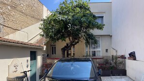 Un coche negro estacionado en una calle estrecha con un árbol y un edificio al fondo.