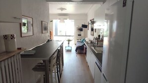 Una cocina estrecha con refrigerador, una mesa de comedor y sillas. Hay una ventana que proporciona luz natural.