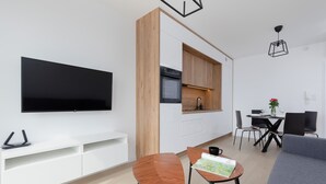 Una sala de estar moderna con televisor de pantalla plana, pared decorativa de madera, zona de comedor con mesa y sillas, y sofá gris.