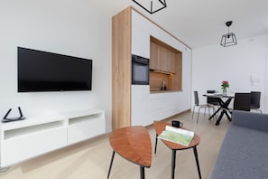 En moderne stue med et fladskærms-tv, en trævæg, et spiseområde med bord og stole, og en grå sofa.