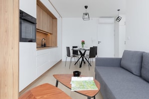 Une cuisine moderne dotée d’appareils électroménagers intégrés, un coin repas avec une table et des chaises, et un canapé gris.