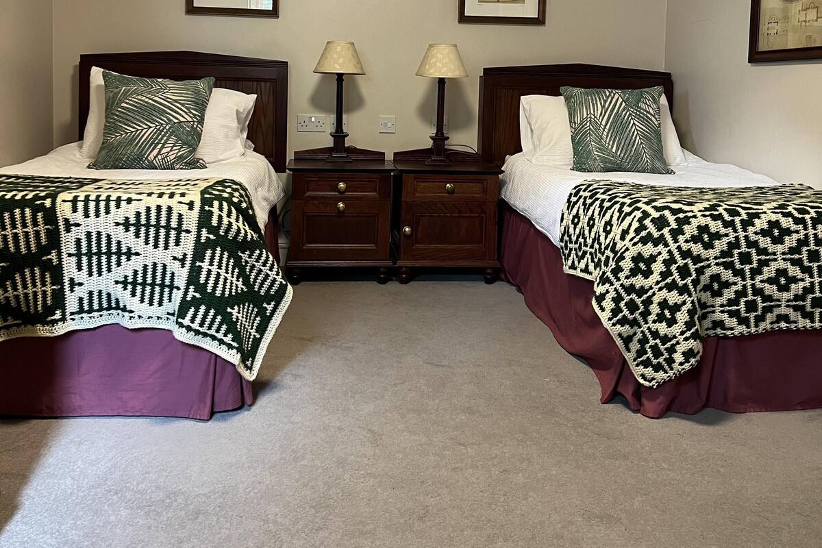 A twin bedroom with two beds, each with a patterned blanket, a nightstand with a lamp, and framed pictures on the wall.