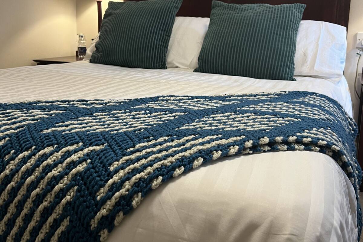 A neatly made bed with a blue and white patterned blanket, two green pillows, and a framed picture on the wall above.