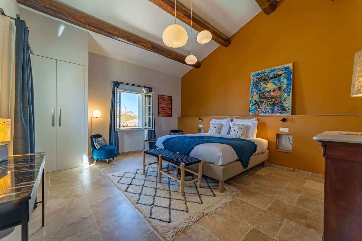 Quarto com cama, cadeira, escrivaninha, janela com cortinas e um quadro na parede.