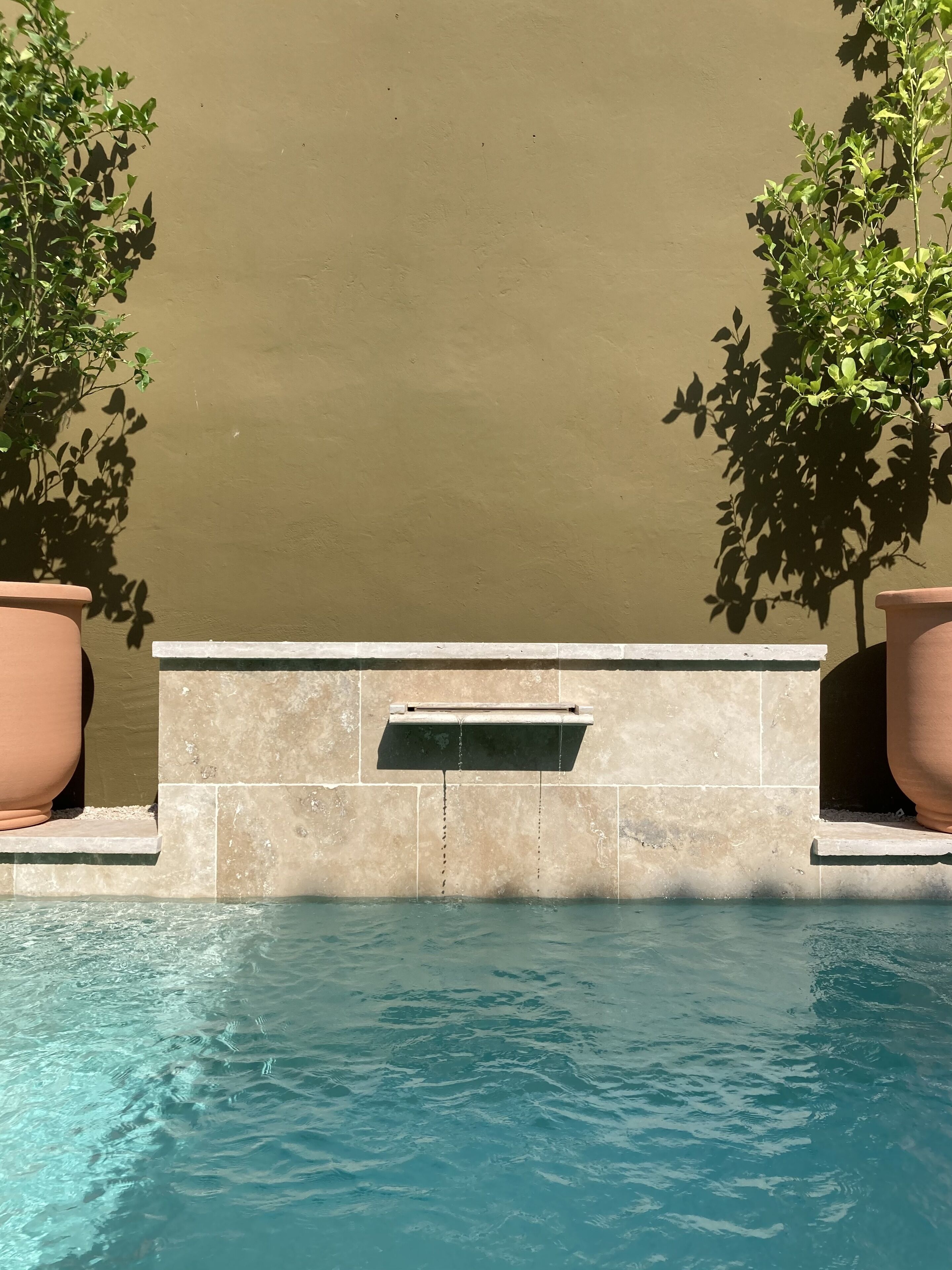 A swimming pool with a stone ledge and a water feature.
