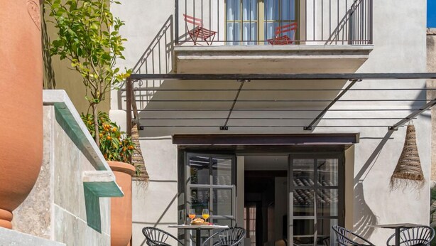 Un espace piscine offrant une vue dégagée sur un immeuble doté d’un balcon, une table avec des chaises et une plante en pot.