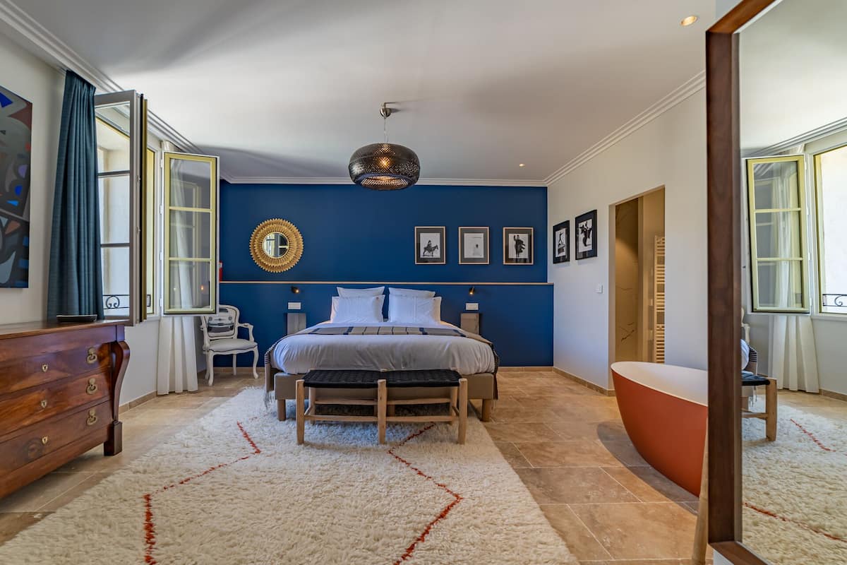 Quarto com cama grande, cómoda de madeira, cadeira, espelho redondo e banheira.
