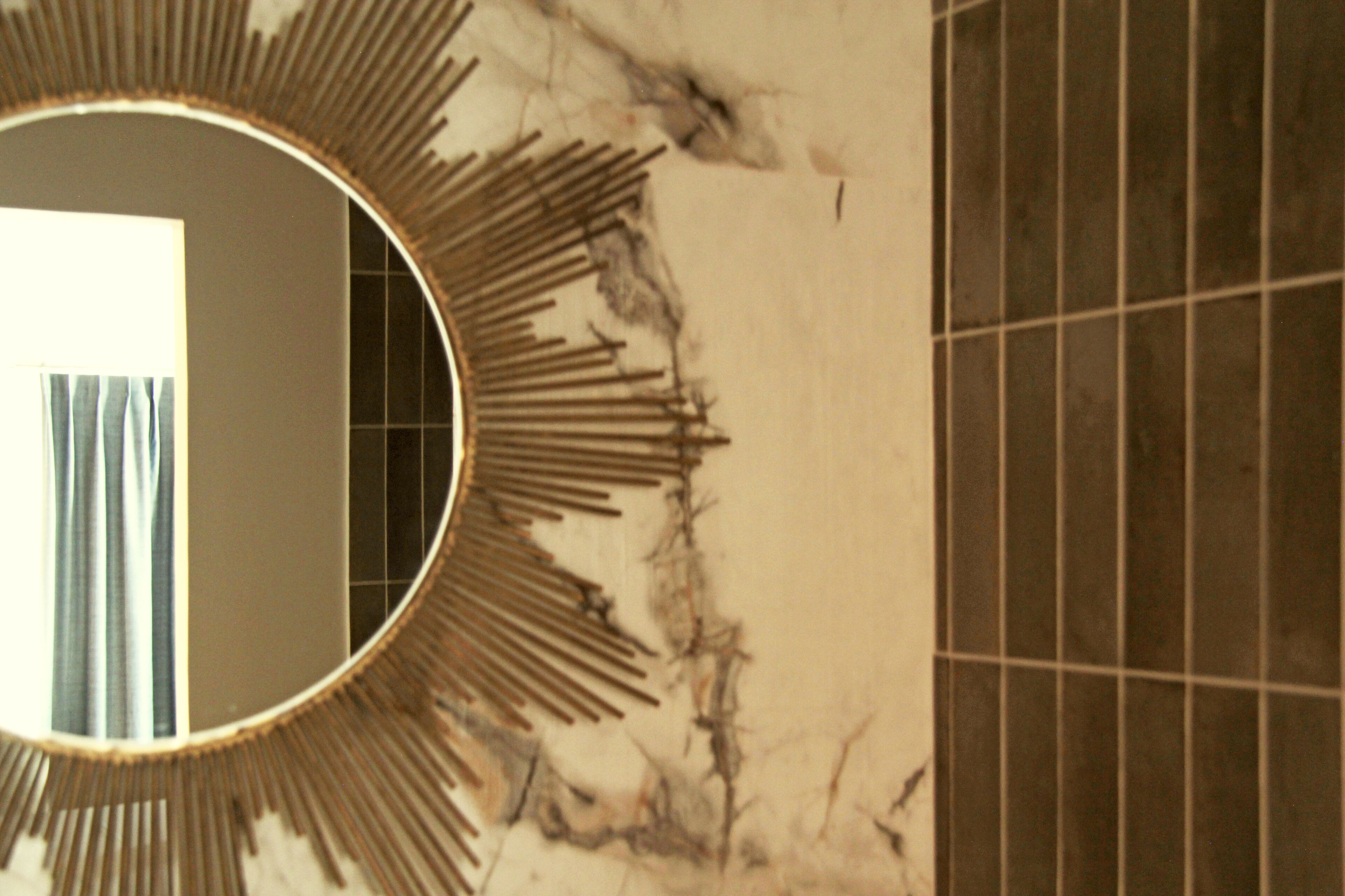 A bathroom with a round mirror, tiled walls, and a marble floor.