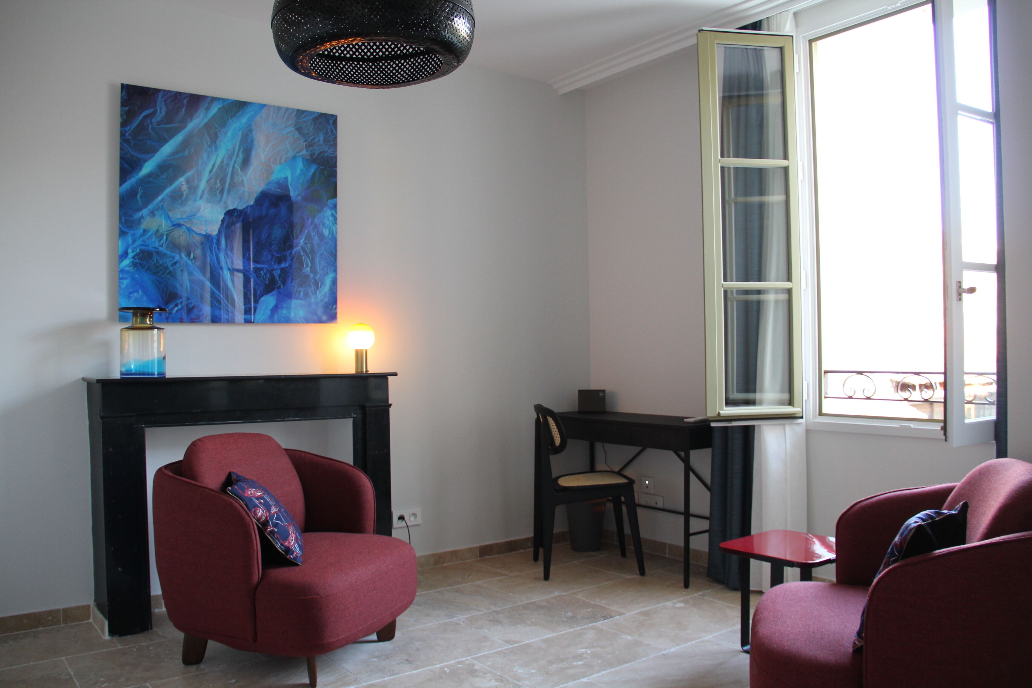 A room with a fireplace, two red armchairs, a desk, and a large window with a view.