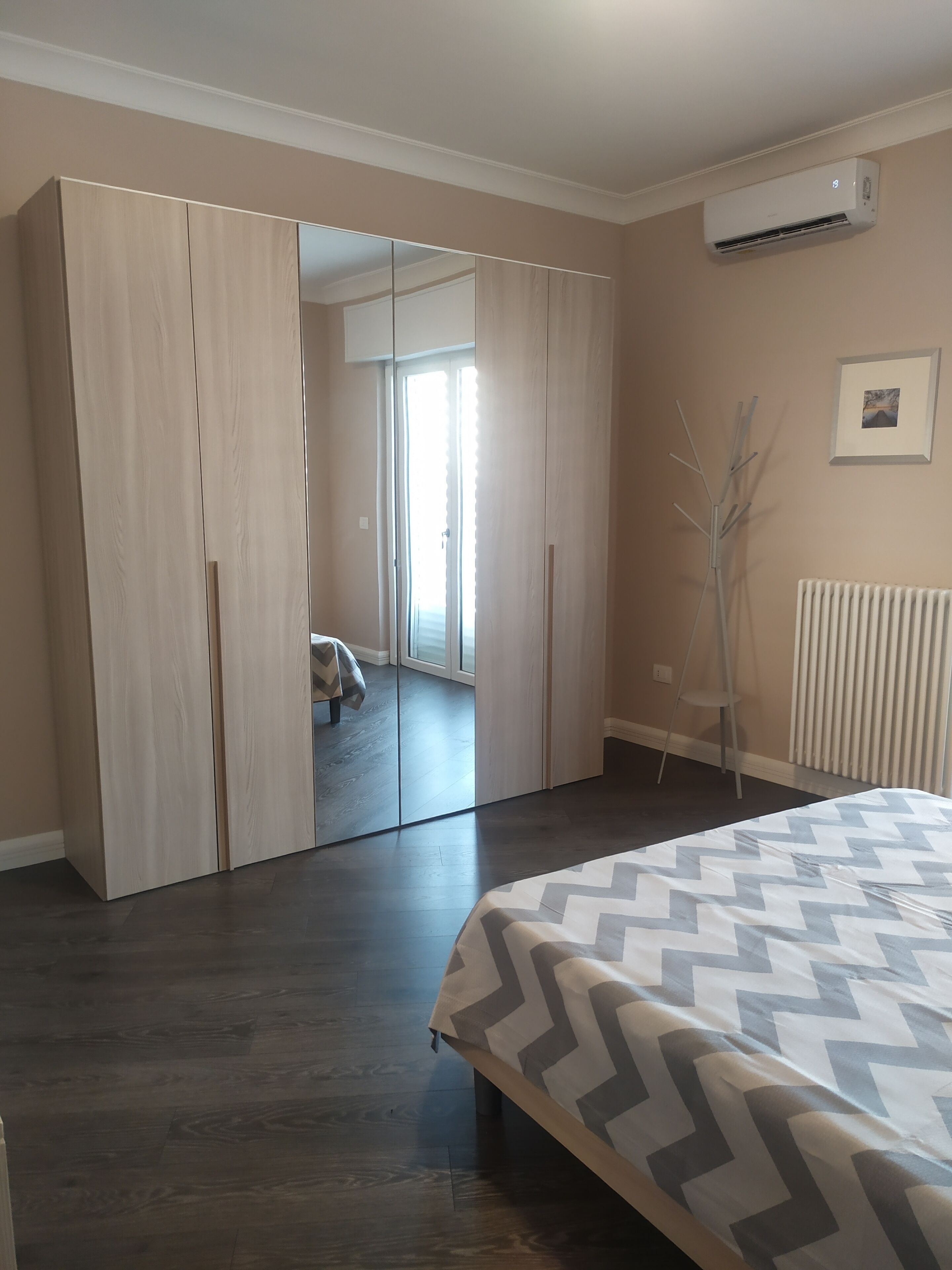 A bedroom with a bed, wardrobe, and an air conditioning unit.