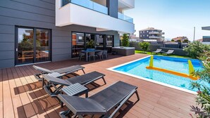 Ein moderner Poolbereich im Freien mit Liegestühlen, einem Whirlpool und einer Holzterrasse.