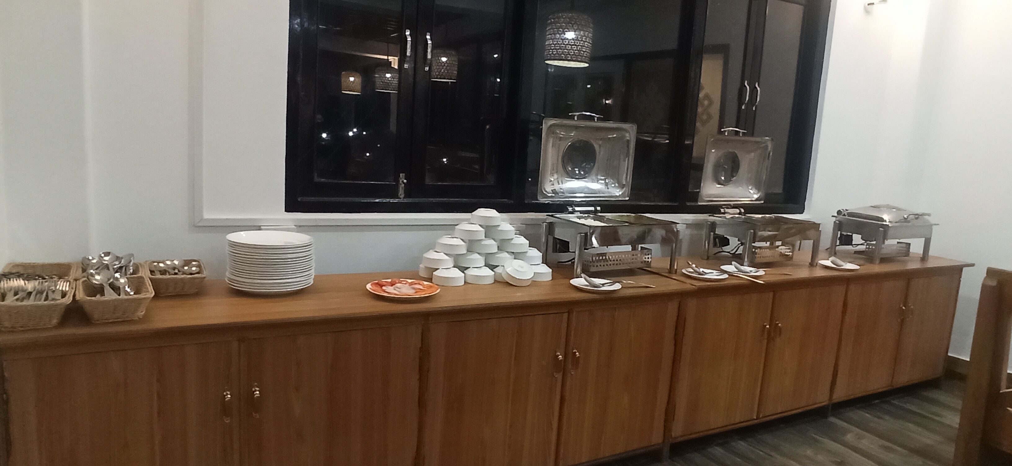 Disposição de buffet com pratos, tigelas e utensílios empilhados sobre um balcão de madeira.