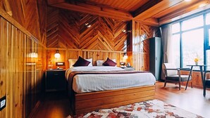 Un dormitorio de cabaña de madera con una cama, mesitas de noche, una silla, una mesa y un ventanal que ofrece vistas al exterior.