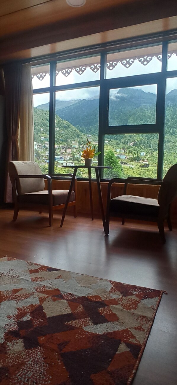 A room with a large window offering a view of a mountainous landscape. There are two chairs and a small table with a potted plant.