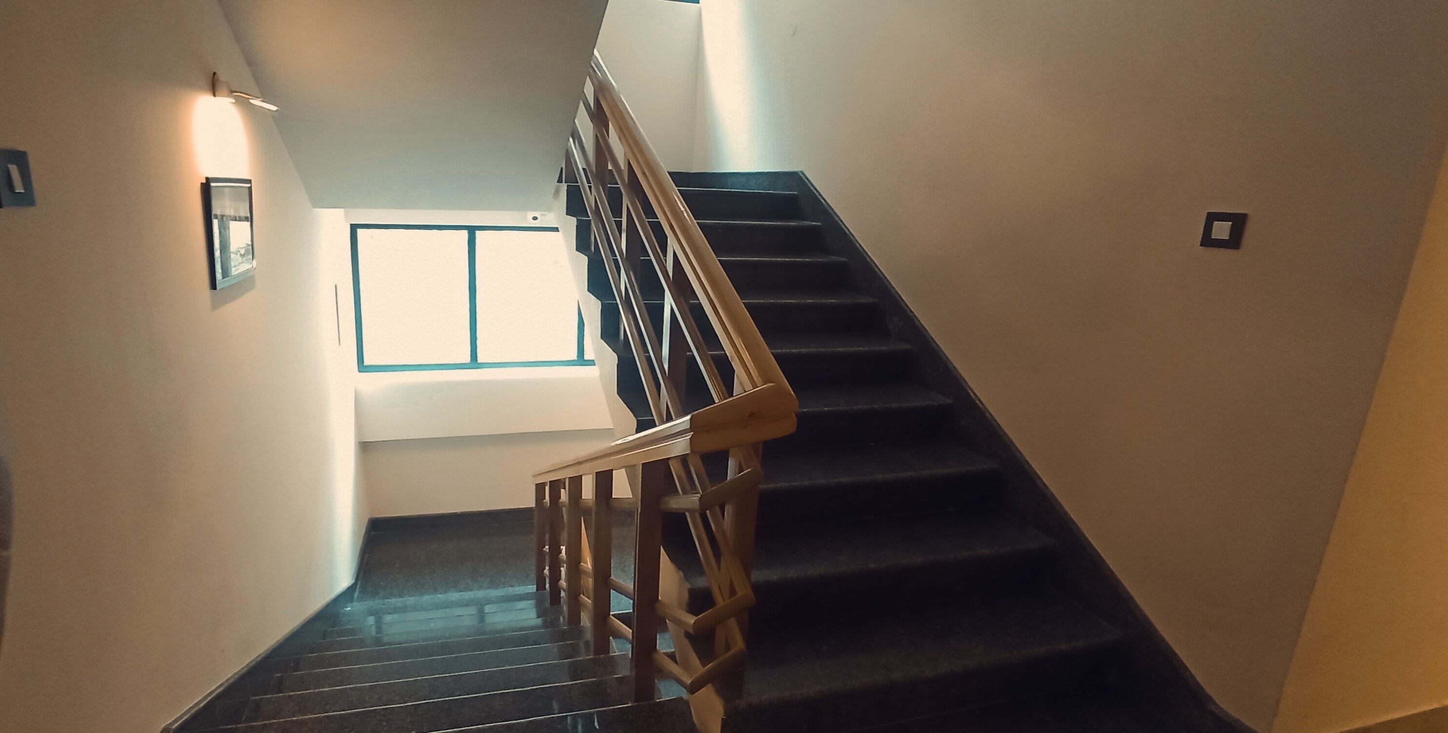 A staircase with wooden handrails and black steps, leading to a landing with a window.