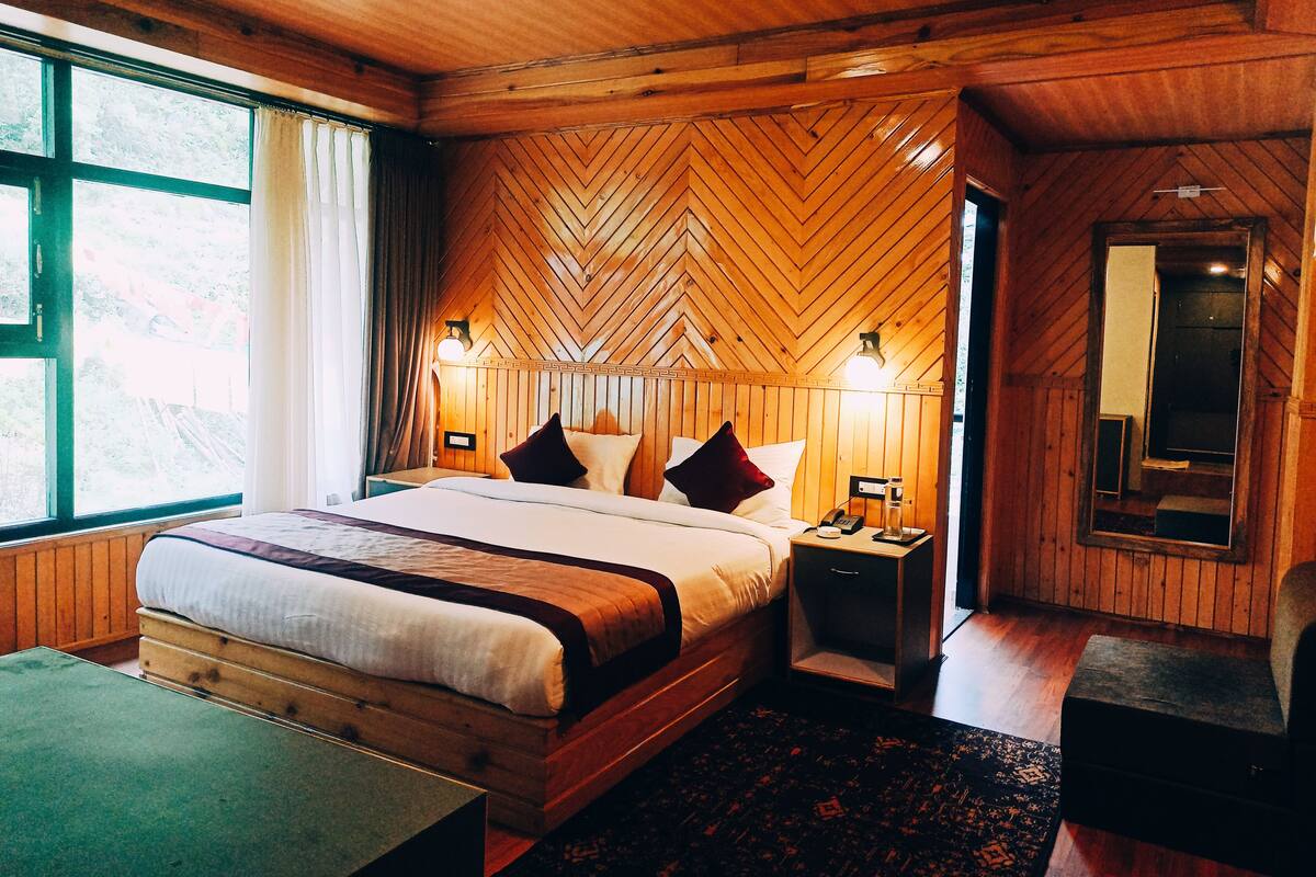 A wooden-paneled bedroom with a large bed, bedside lamps, a mirror, and a view of the outdoors.