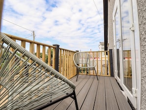 A wooden deck with a wicker chair and a glass door leading to a building. - Westcott (Skegness)