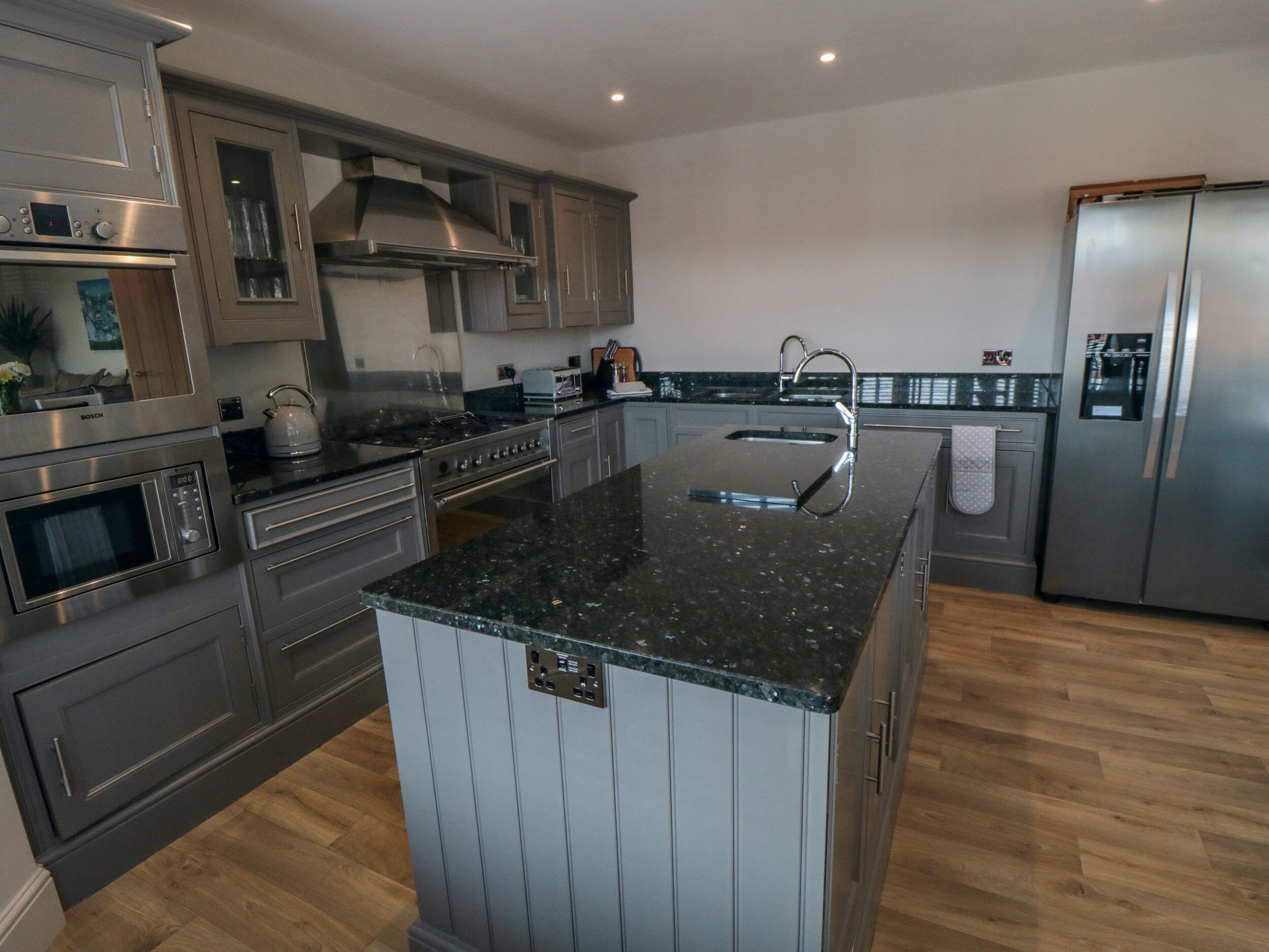 A modern kitchen with stainless steel appliances, a granite countertop, and wooden flooring.