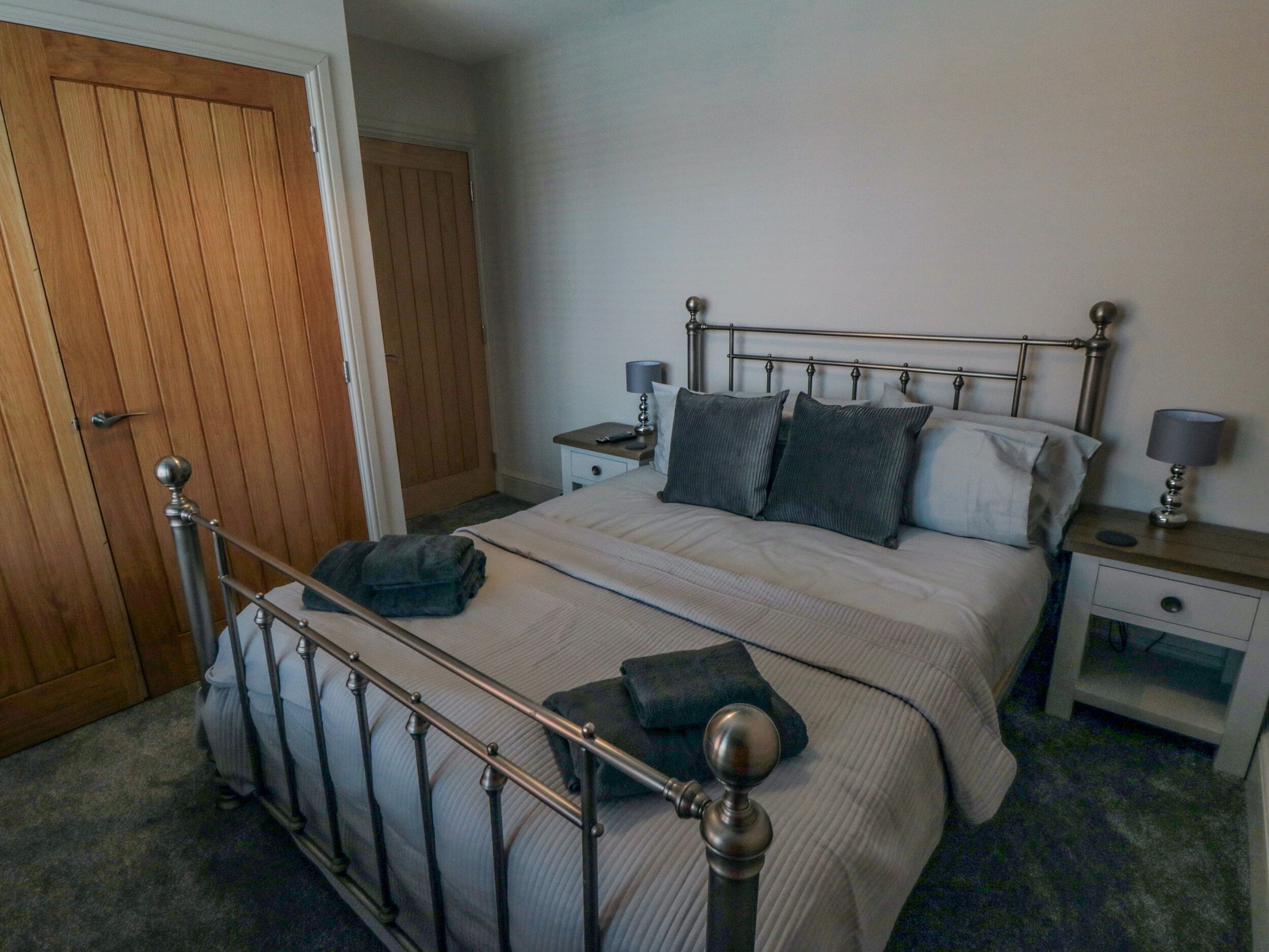Une chambre à coucher avec un lit à ossature métallique, une porte en bois et une table de chevet avec une lampe.