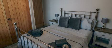 A bedroom with a metal-framed bed, a wooden door, and a nightstand with a lamp.
